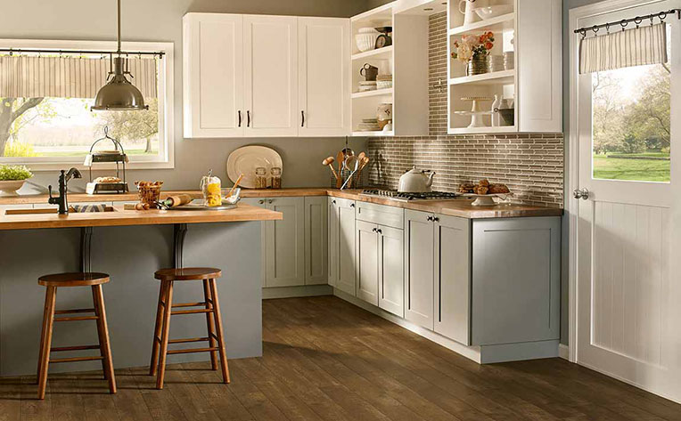 A kitchen with island and bar seating, white overhead cabinets, and grey lower cabinets that accentuate the wood floors.