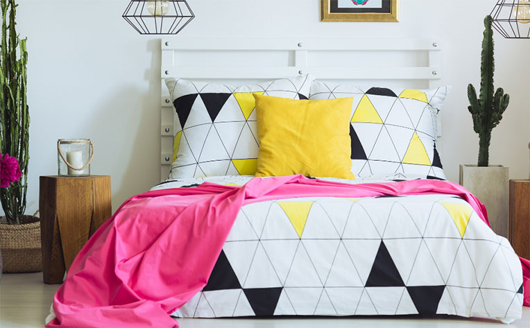 Bedroom with two pendulum lights over and a bed covered in sheets inspired by the Memphis design movement.